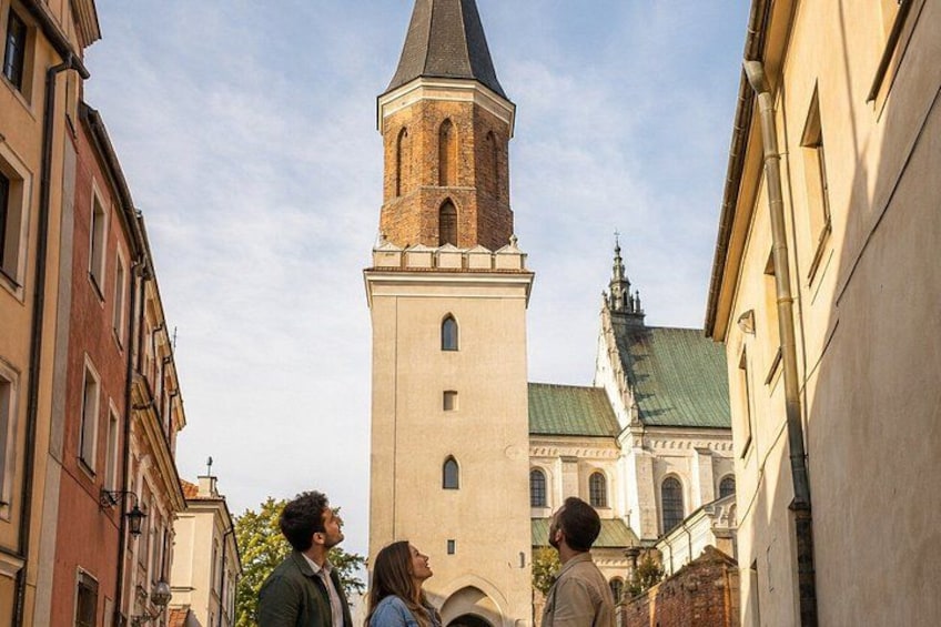 Una torre histórica, una iglesia con techo verde y edificios colindantes en una calle estrecha. 4