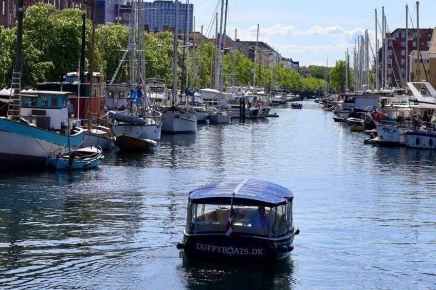 A marina with various sailboats docked along a narrow waterway, surrounded by buildings and trees. 3