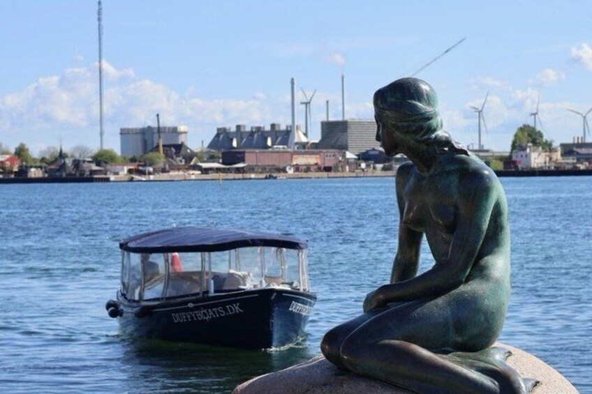 A statue of a seated figure by a body of water with a boat in the background. 1