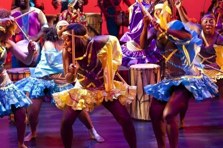 A group of dancers in colorful costumes performing on stage with drums. 3