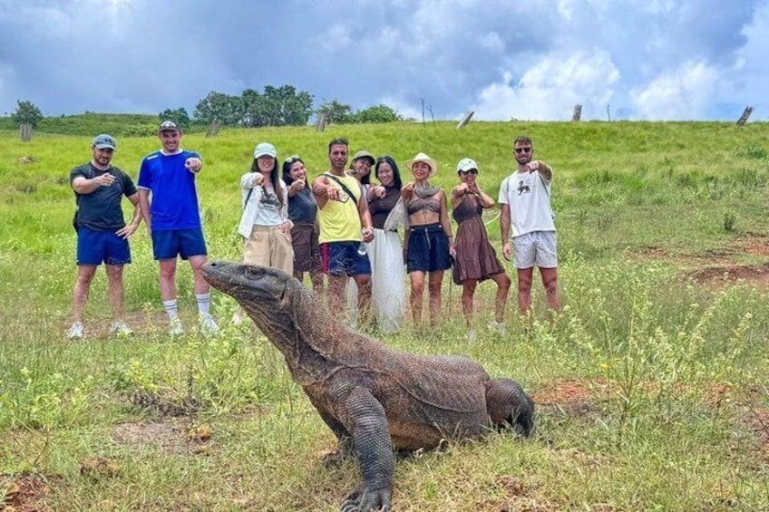 A group of people standing in a grassy field with a Komodo dragon in the foreground. 5