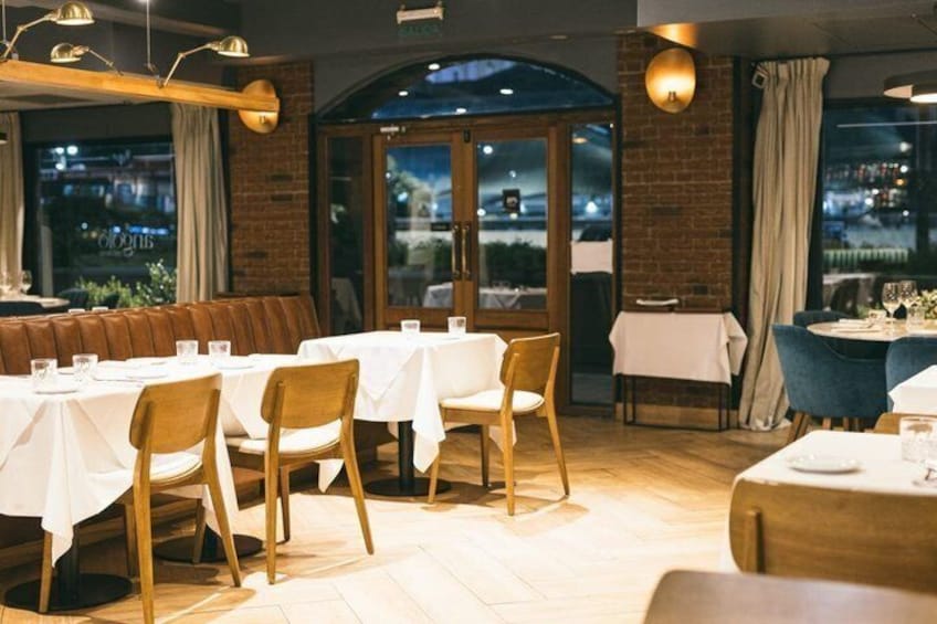 Un restaurante con mesas y sillas de madera, paredes de ladrillo y vistas a la ciudad de noche. 5