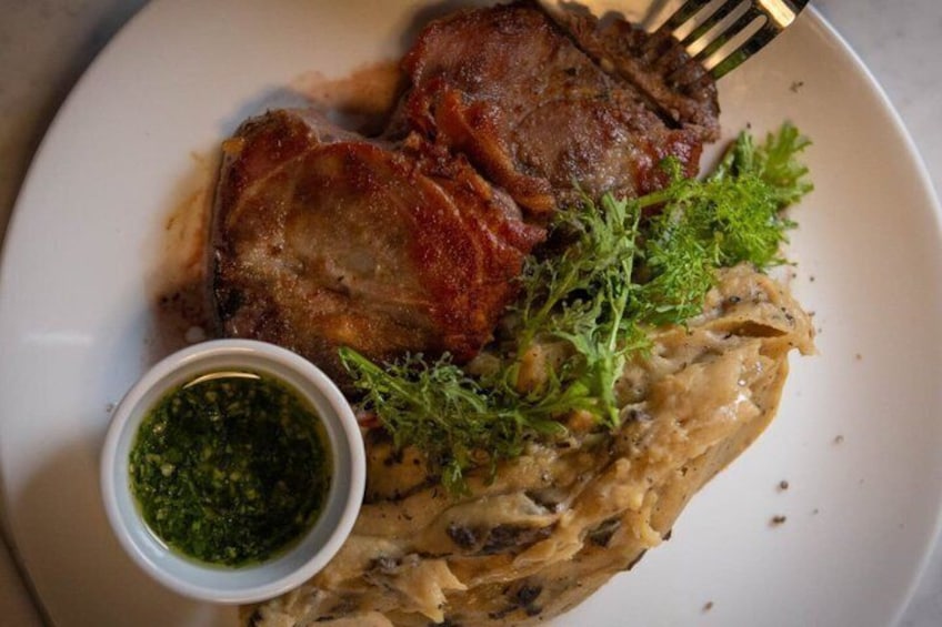 Un plato con un trozo de carne, posiblemente cerdo, adornado con vegetales y acompañado de salsa. 4