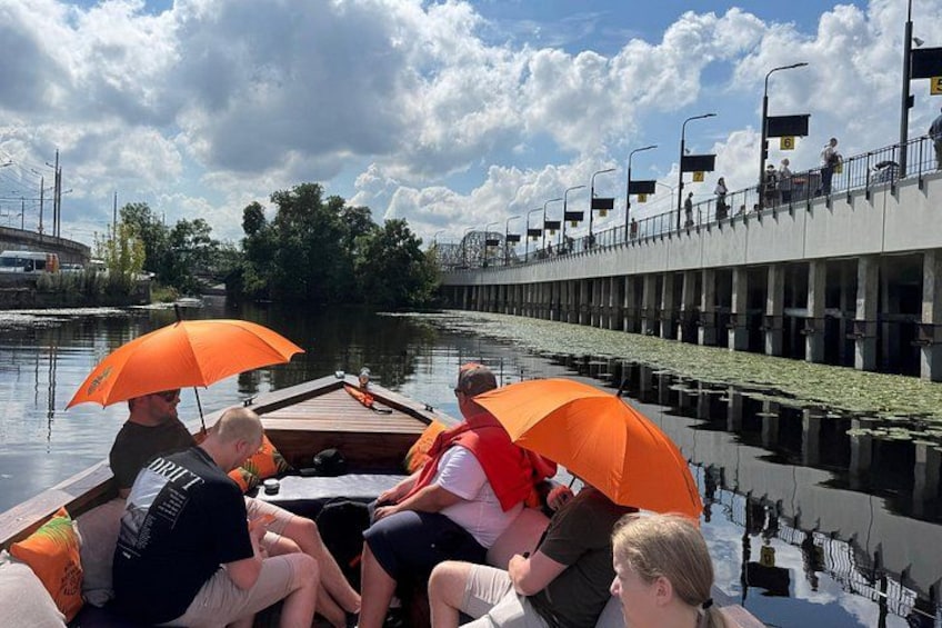 A group of people on a boat with orange umbrellas, a river, and a bridge in the background. 3