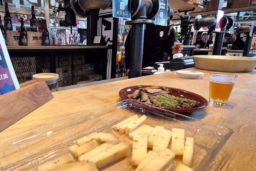 A wooden table with a plate of food, a glass of beer, and a cutting board with cheese. 5