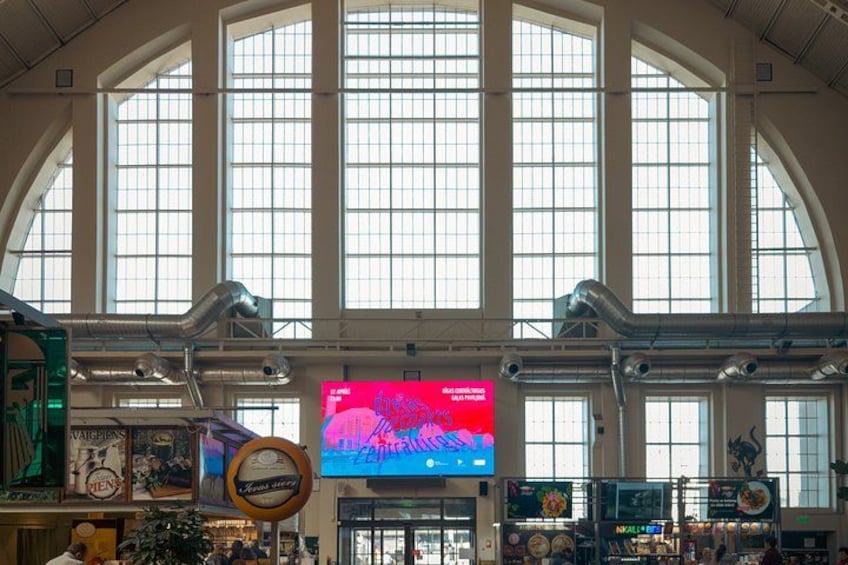 A spacious indoor area with large arched windows, a digital display, and various signs and advertisements. 4