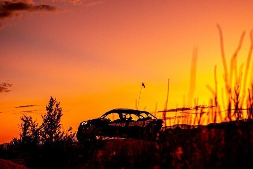 Een auto in silhouette voor een ondergaande zon, met een vlag erop. 1