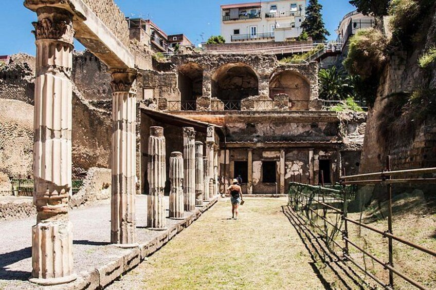 Des ruines antiques avec des colonnes et des arches, une personne qui marche et un bâtiment en arrière-plan. 5