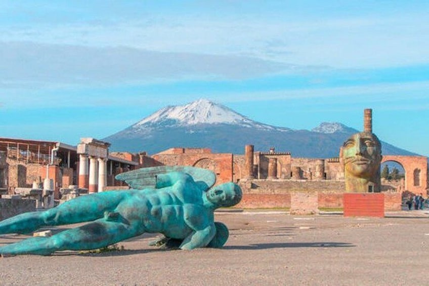 Une grande statue de bronze représentant une figure allongée, des ruines antiques et une montagne en arrière-plan. 3