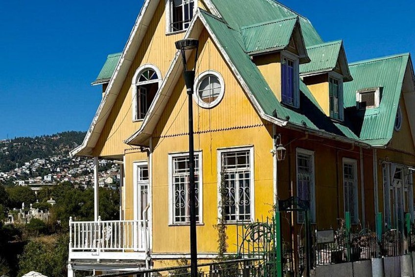 Et gult hus med grønt tag, hvide vinduer og en balkon. 5