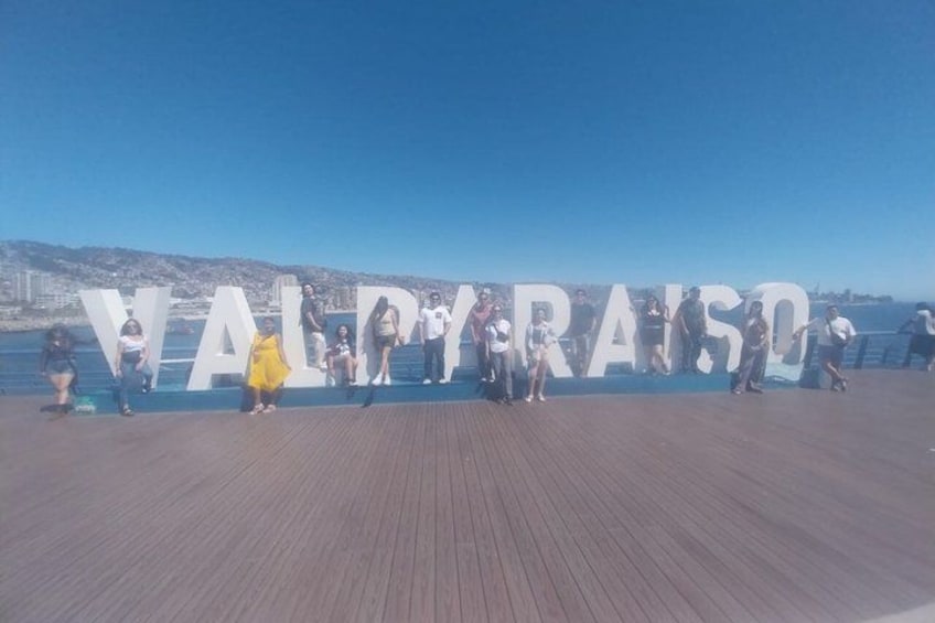 En strandpromenad med folk som står framför en stor skylt där det står ”VALPYRAIS”. 3