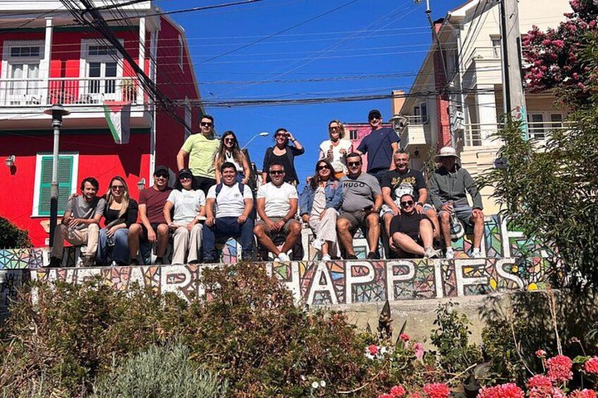 Un grupo de personas posando frente a un letrero colorido con el texto 'THE ARTS OF HAPPINESS'. 2