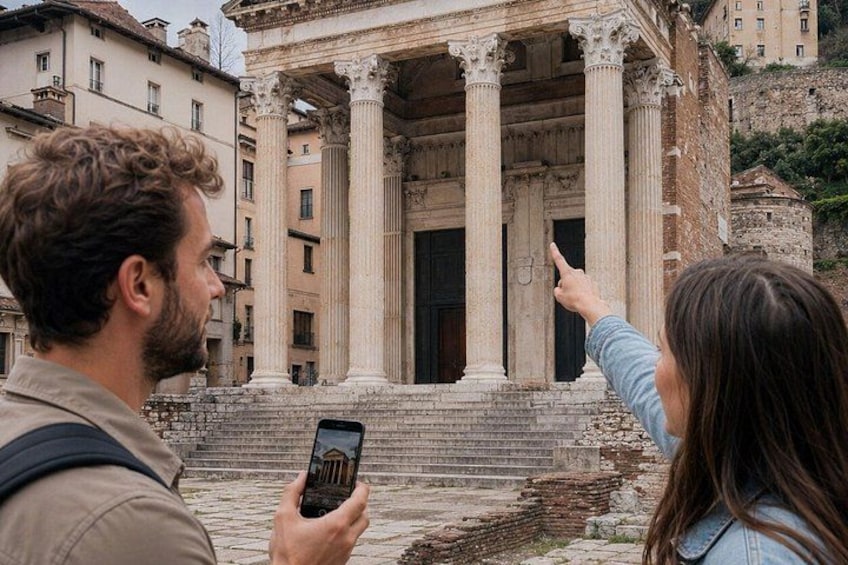 A classical building with columns, a person taking a photo, and another pointing at it. 1