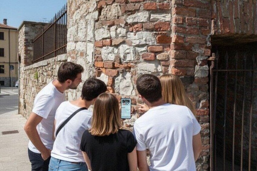 Un groupe de personnes se tient près d’un mur de pierre surmonté d’un portail en métal. 5