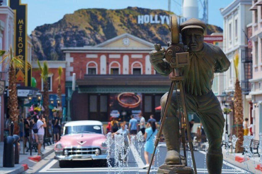A statue of a man with a camera on a tripod, a vintage car, and a building with 'HOLLYWOOD' sign. 1