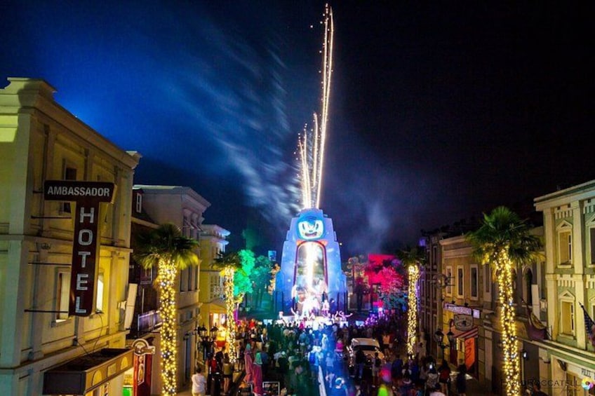 Una calle bien iluminada con un letrero grande, edificios y palmeras. 3