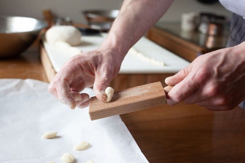 Hands shaping dough with a wooden tool on a kitchen counter. 4