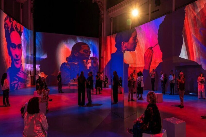 Eine Innenraum-Kunstausstellung mit großen digitalen Projektionen und zahlreichen Besuchern. 3