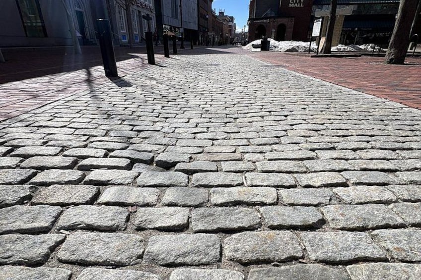 A cobblestone street with brick buildings and a clear sky. 2