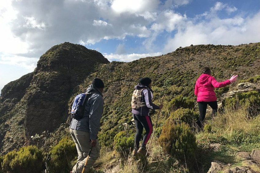 Tres excursionistas en un sendero montañoso con terreno rocoso y vegetación escasa. 2