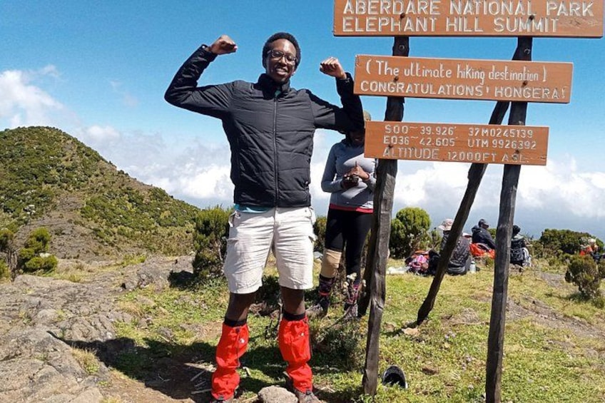 Una persona de pie al pie de un cartel con información sobre el Parque Nacional Aberdare y la Cumbre Elephant Hill. 3