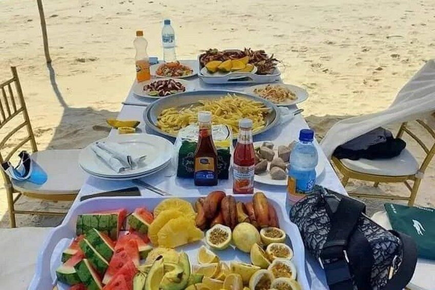 En måltidsplats uppdukad på stranden med tallrikar, mat, dryck och en kylväska. 1