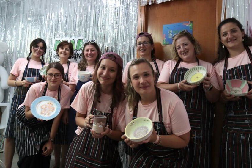 A group of people in aprons holding plates and a mug, standing in front of a shiny backdrop. 4