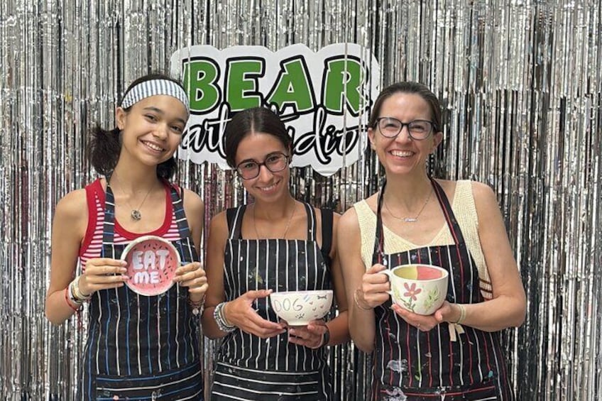 Three people holding bowls with food, standing in front of a metallic backdrop with the word 'BEAR' visible. 2
