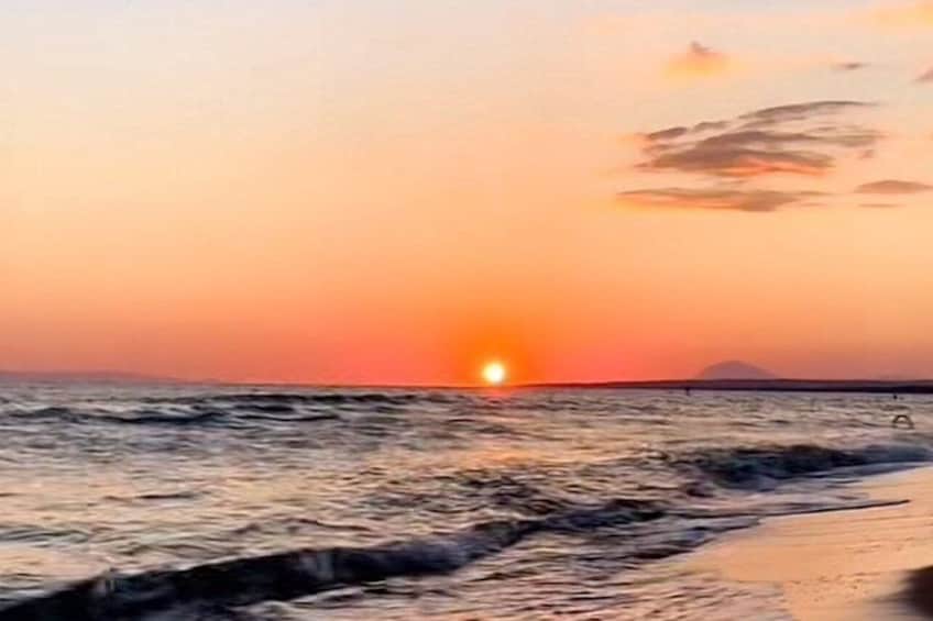 Ein Sonnenuntergang über dem Meer mit Wellen und einer entfernten Landmasse. 2