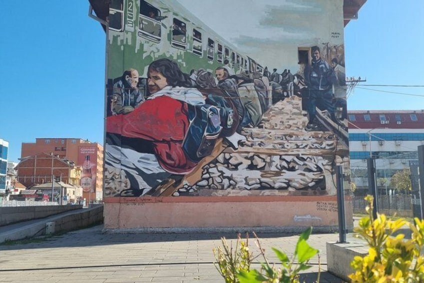 A mural of people ascending stairs with a train in the background. 1