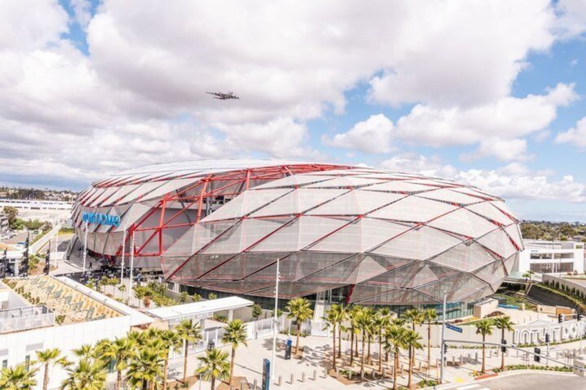 Ein großes, modernes Stadion mit markanter rot-weißer Struktur, umgeben von Palmen und blauem Himmel. 2