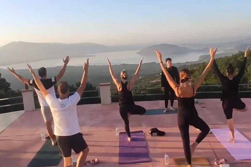 A group of people performing yoga on mats with a scenic view of mountains and a body of water. 1