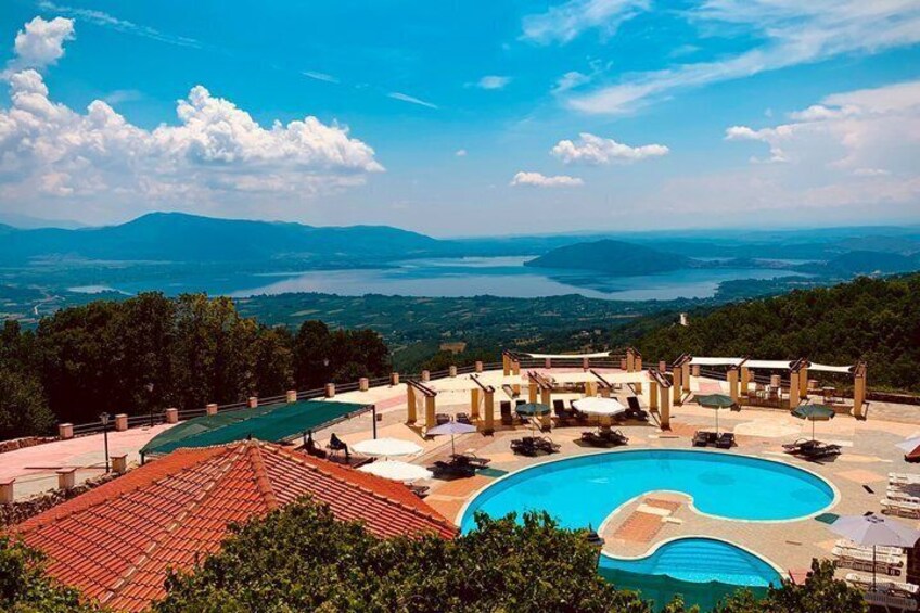 A pool with lounge chairs and umbrellas, surrounded by trees and a view of distant mountains and water. 4