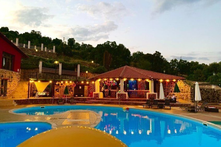 A swimming pool with a bar area, surrounded by stone walls and a hill in the background. 3
