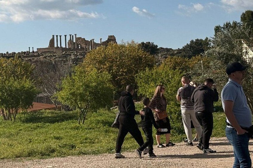 Eine Gruppe von Menschen geht auf einem Pfad, im Hintergrund sind Ruinen zu sehen. 5