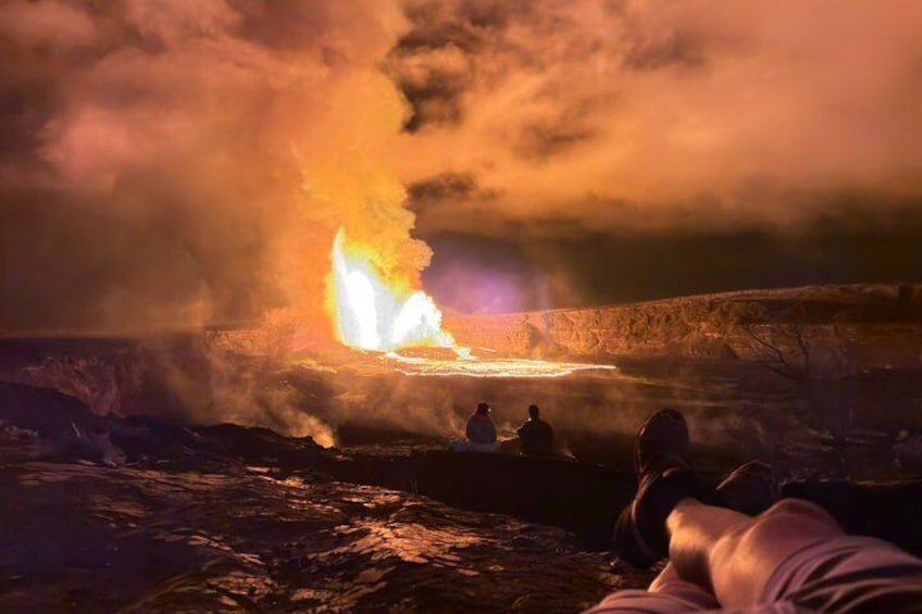 A volcanic eruption with lava flowing, people observing from a distance, and a dramatic sky. 1
