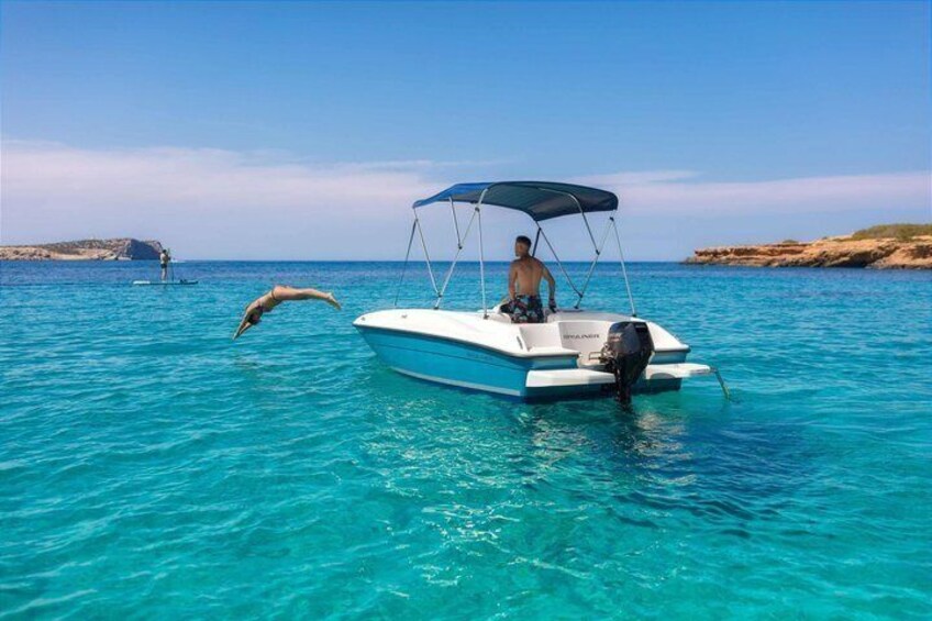 A boat with a canopy on a turquoise sea, a dolphin leaping, and a distant paddleboarder. 1