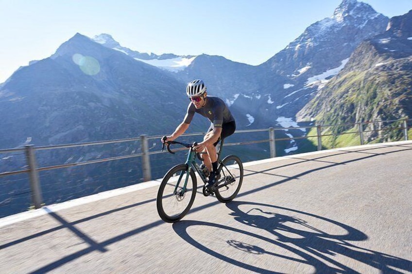 A cyclist riding a road bike on a paved path with a mountainous landscape in the background. 5