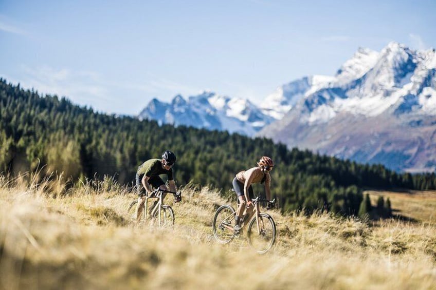 Two cyclists on a trail with a mountainous backdrop. 4