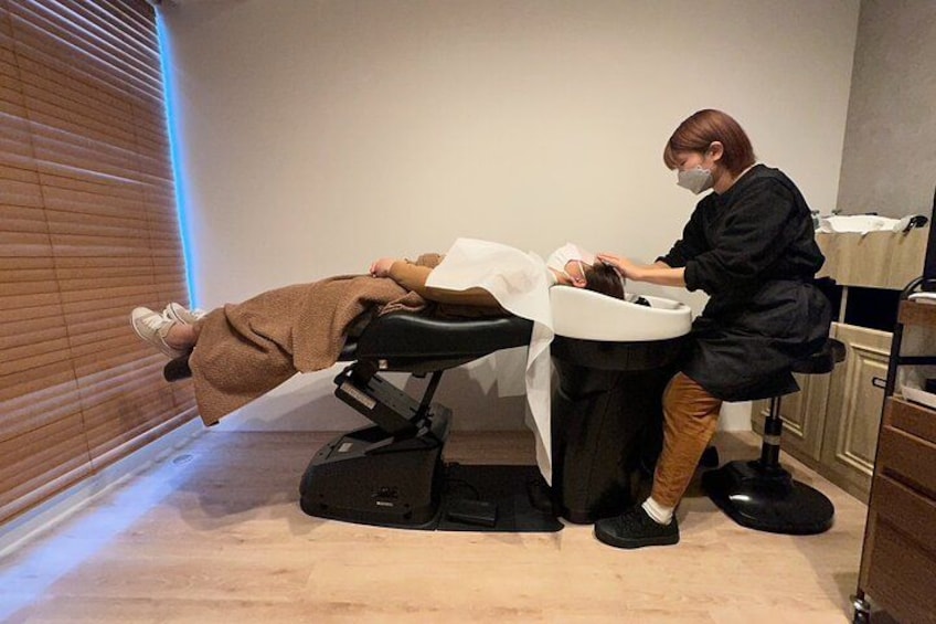 En person ligger på en behandlingsstol och får en hårbehandling av en professionell frisör. 4