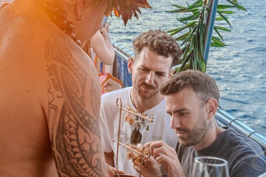 En person med tatueringar, en man med lockigt hår och en annan man som håller i ett glas på en båt. 2