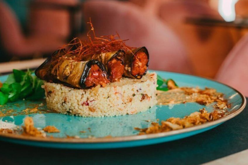 Un plat composé d’une aubergine farcie, servie sur un lit de riz et agrémentée de filaments rouges, le tout présenté dans une assiette bleue. 3
