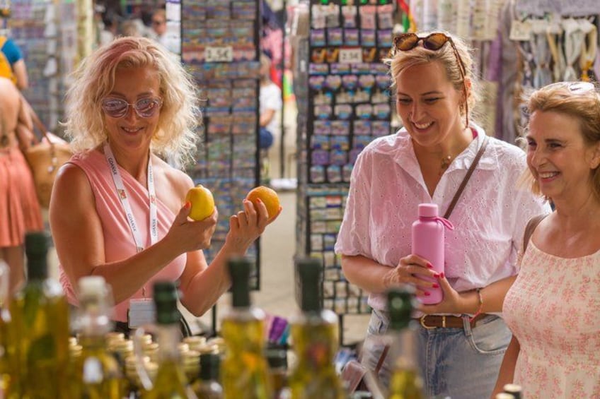 Twee personen bekijken citroenen op een markt, met verschillende producten op de achtergrond. 1