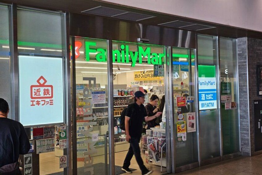 En FamilyMart-butik med en entré av glas, en synlig bankomat och en person som går förbi. 2
