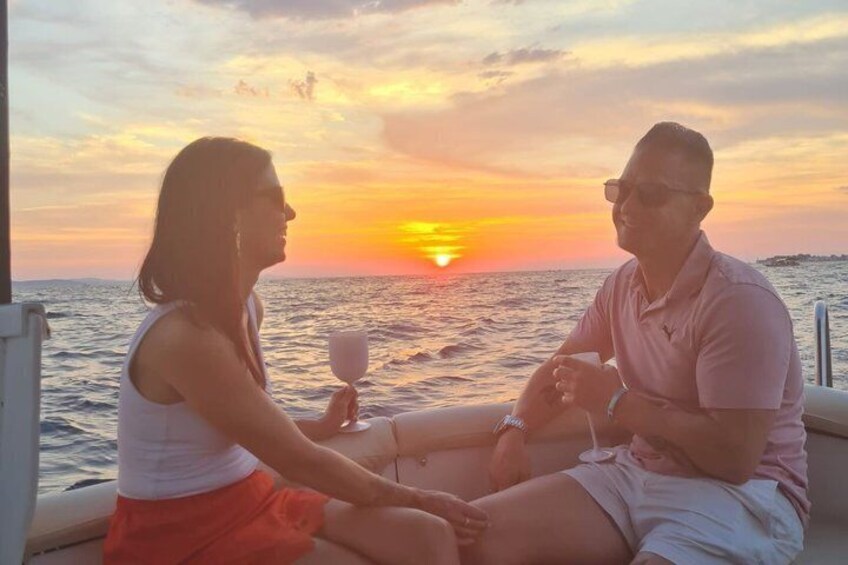 Two people sitting on a boat, facing the sunset over the ocean. 2