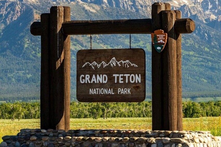 En träskylt med texten ”GRAND TETON NATIONAL PARK” och en illustration av ett bergskedja. 1