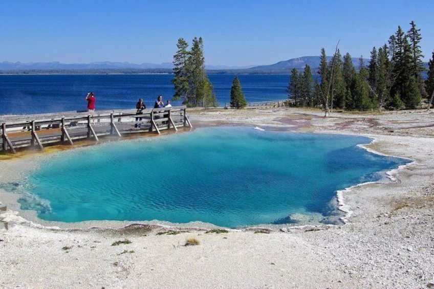 A clear blue lake with a wooden dock, surrounded by trees and mountains in the background. 4