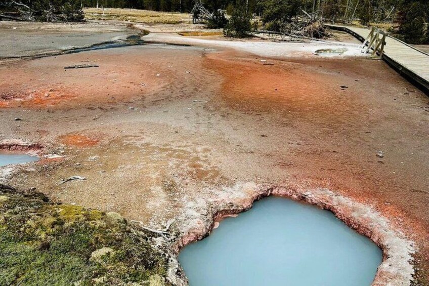 Ein geothermisches Gebiet mit einem großen, blauen Becken, umgeben von rötlich-brauner Landschaft. 3