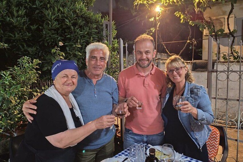 Quattro persone all'aperto di notte, con bevande in mano, con un tavolo e delle sedie in primo piano. 1