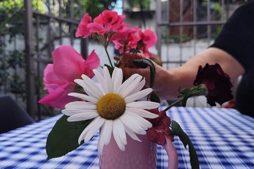Una mesa con un mantel a cuadros, un jarrón con una margarita blanca, flores rosadas y una rosa roja. 2